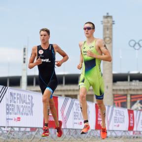 Zwei Triathleten laufen gemeinsam im Hintergrund sind die Olympischen Ringe zu sehen