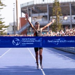 Eine Triathletin läuft mit zum Jubel hochgerissenen Armen als Erste auf das Zielband zu