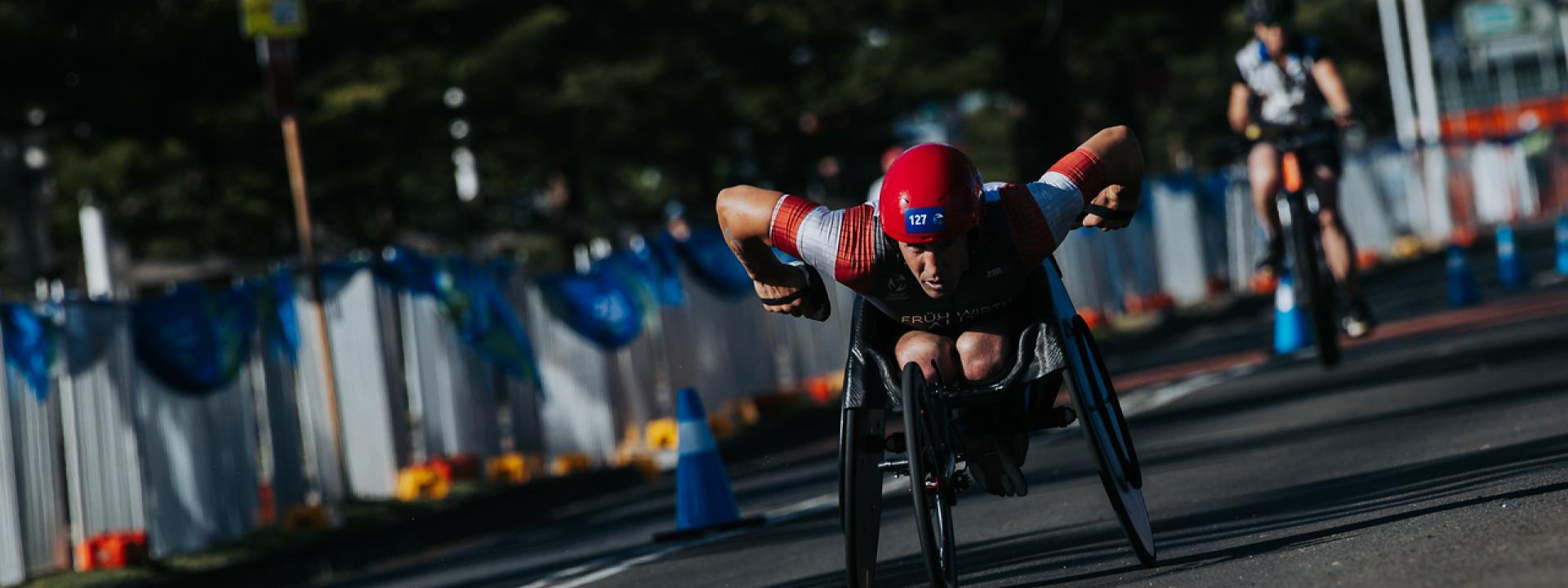 Ein Para Triathlet fährt schnell mit seinem Rollstuhl auf einer asphaltierten Straße