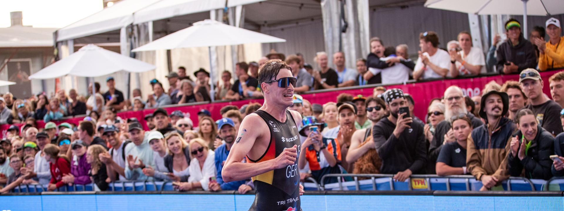 Ein deutscher Triathlet läuft die letzten Meter über den blauen Teppich vor jubelnden Zuschauern ins Ziel