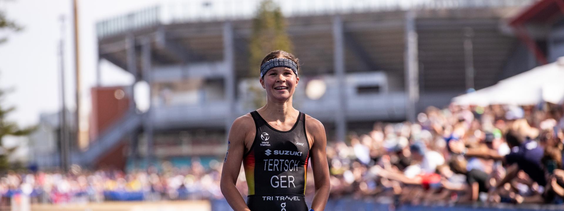 Eine siegreiche Sportlerin steht glücklich im Zielbereich einer Triathlonstrecke