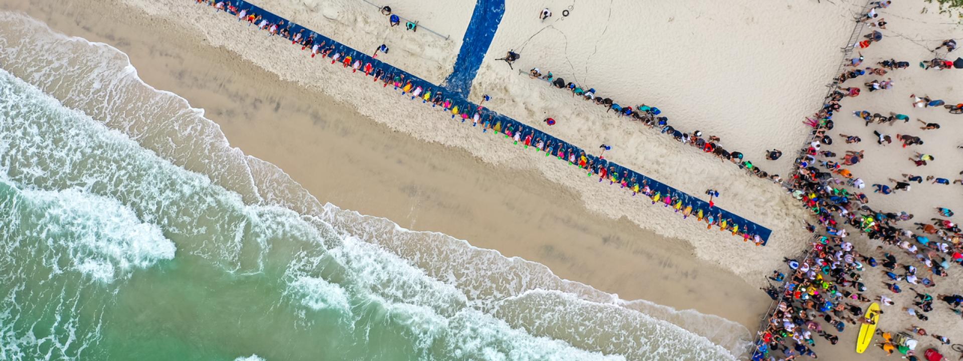 aus der Vogelperspektive sieht man Meer und Strand und einen blauen Teppich auf dem Sand, der die Startlinie für Athleten ist