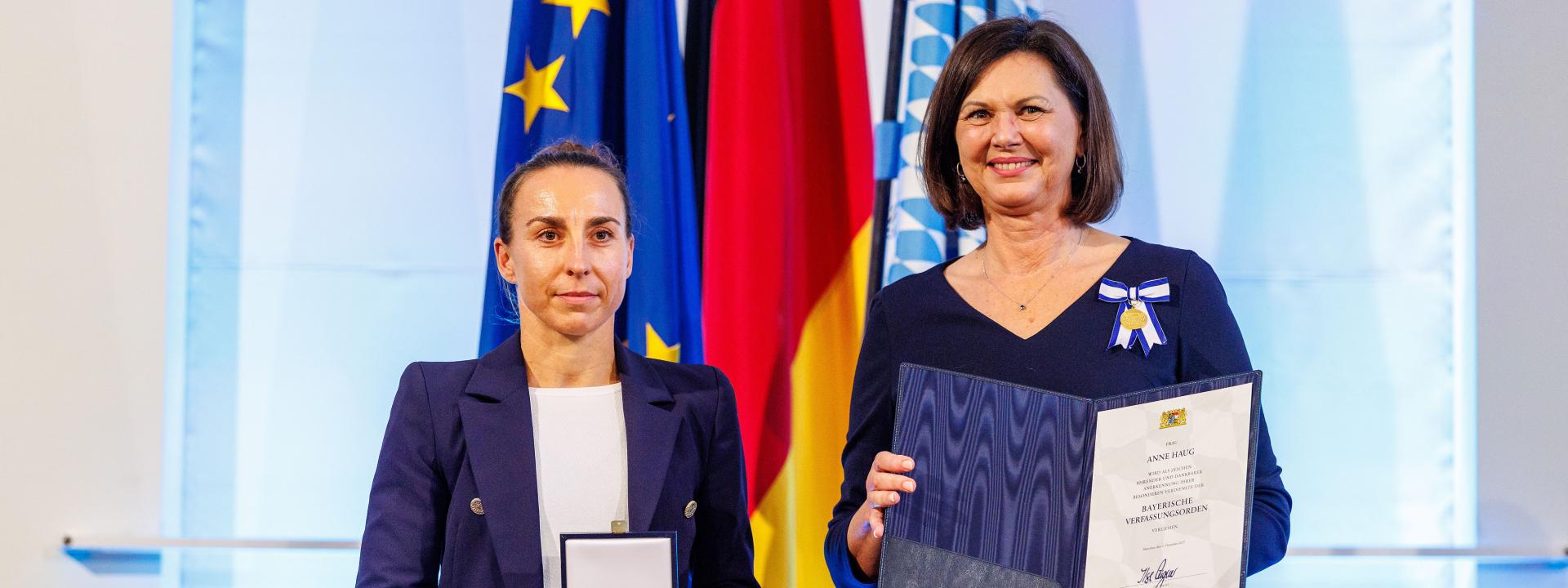 Eine geehrte Preisträgerin präsentiert gemeinsam mit ihrer Laudatorin eine Urkunde und eine Medaille