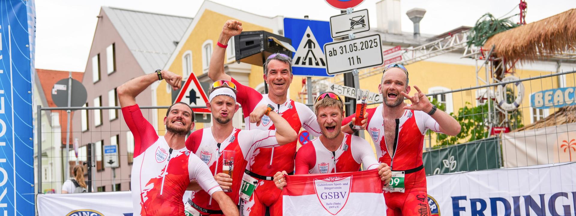 Fünf Triathleten jubeln gemeinsam im Zielbereich einer Veranstaltung posierend in die Kamera