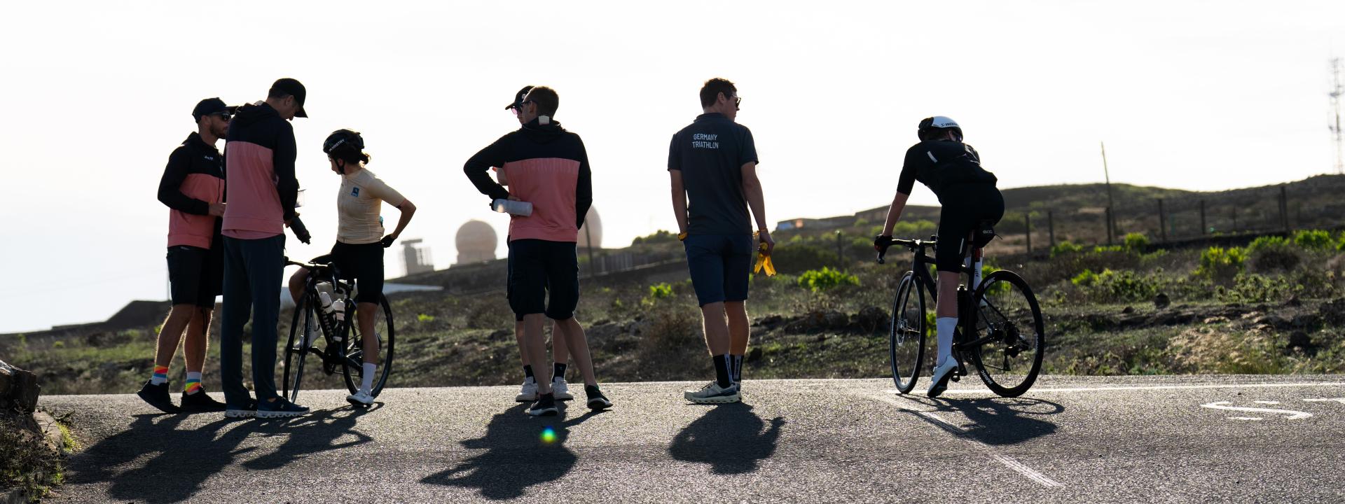 Männliche und weibliche Sportlerinnen und Sportler mit Rennrad analysieren gemeinsam mit mehreren Trainern eine Einheit