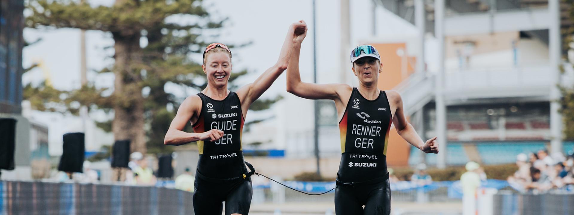Zwei Triathletinnen überqueren gemeinsam, sich an der Hand haltend die Ziellinie