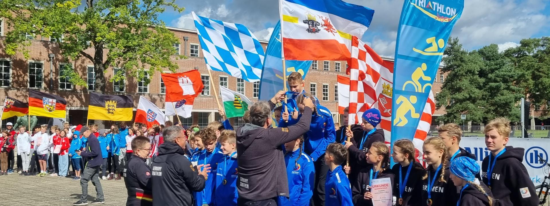 Siegerehrung des Gewinnerteams aus Bremen, im Hintergrund halten viele Fahnen hoch 