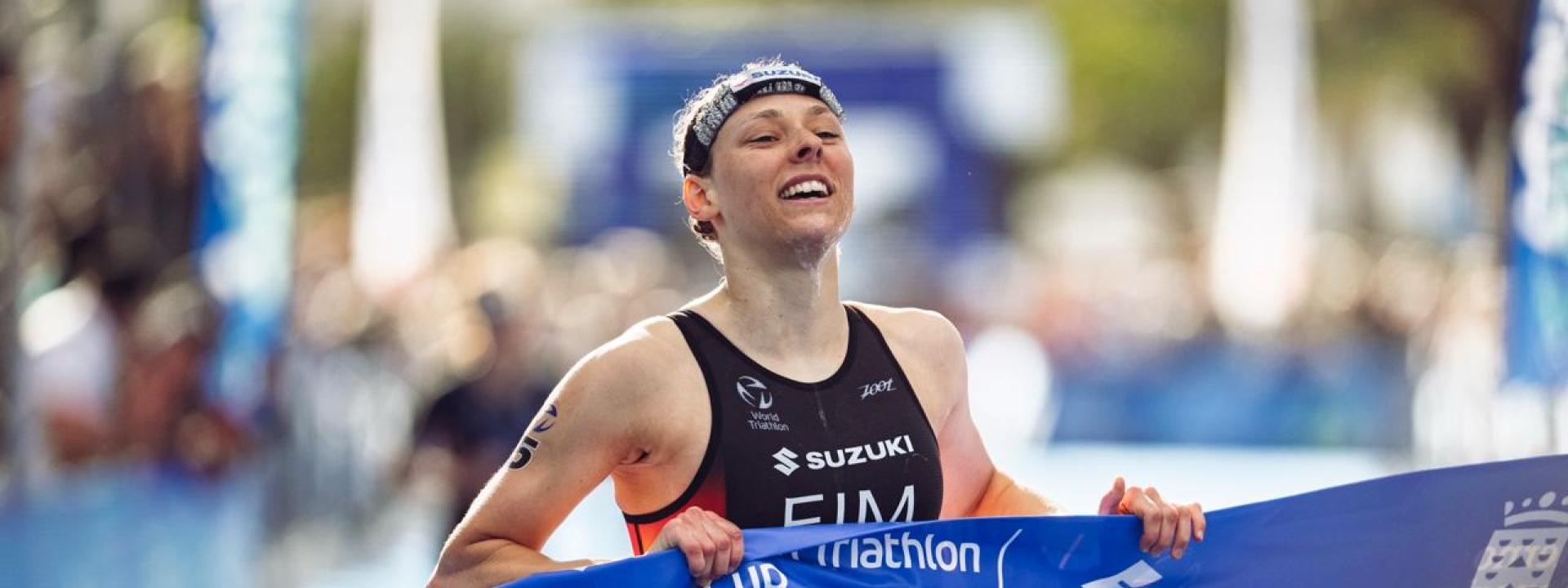 Eine Triathletin läuft glücklich mit dem Zielband in der Hand zum Sieg