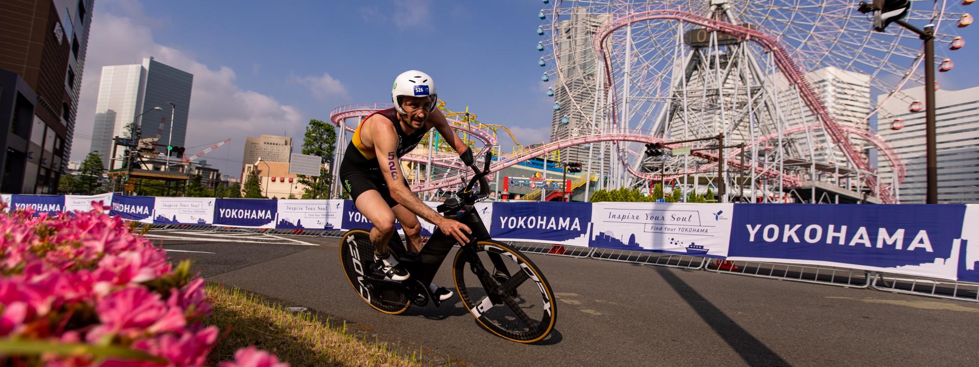 Ein deutscher Para Triathlet fährt mit dem Rad eine Kurve, im Hintergrund ist ein Riesenrad zu sehen