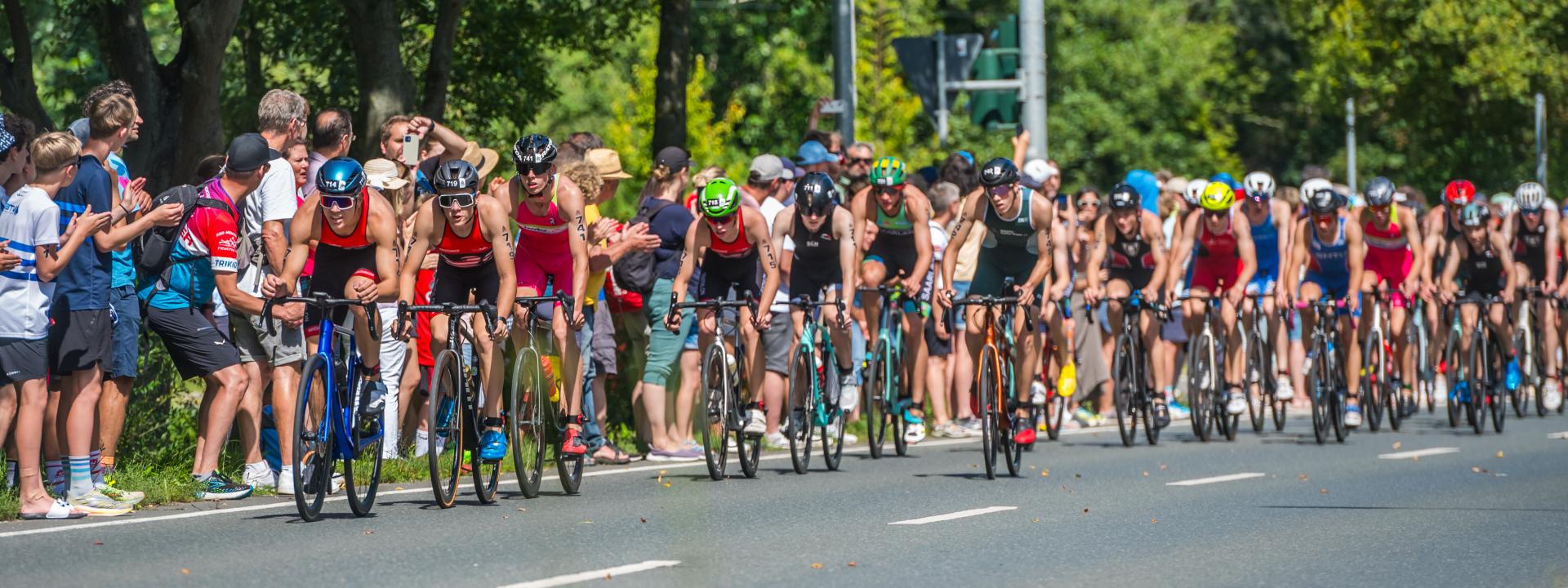 Junge Athleten auf dem Fahrrad im Windschatten, an der Strecke stehen viele Zuschauer