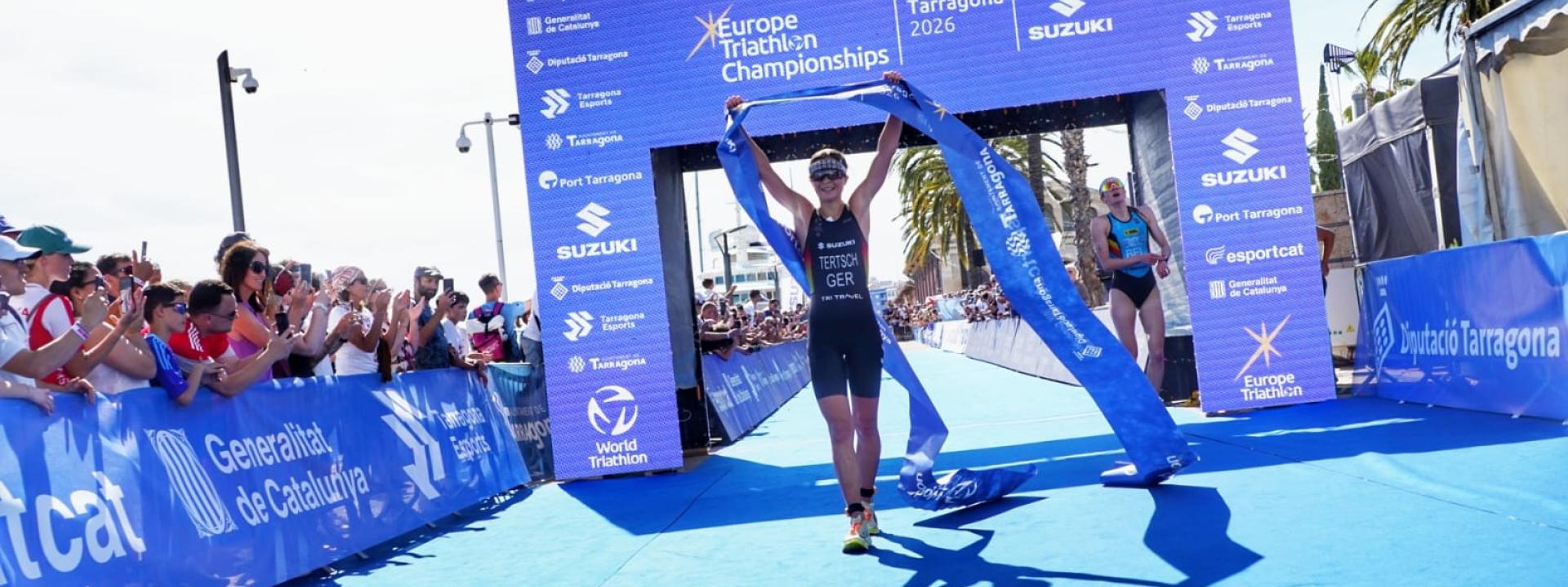 Triathletin läuft mit hochgestreckten Armen und Zielbanner in den Händen unter Zielbogen