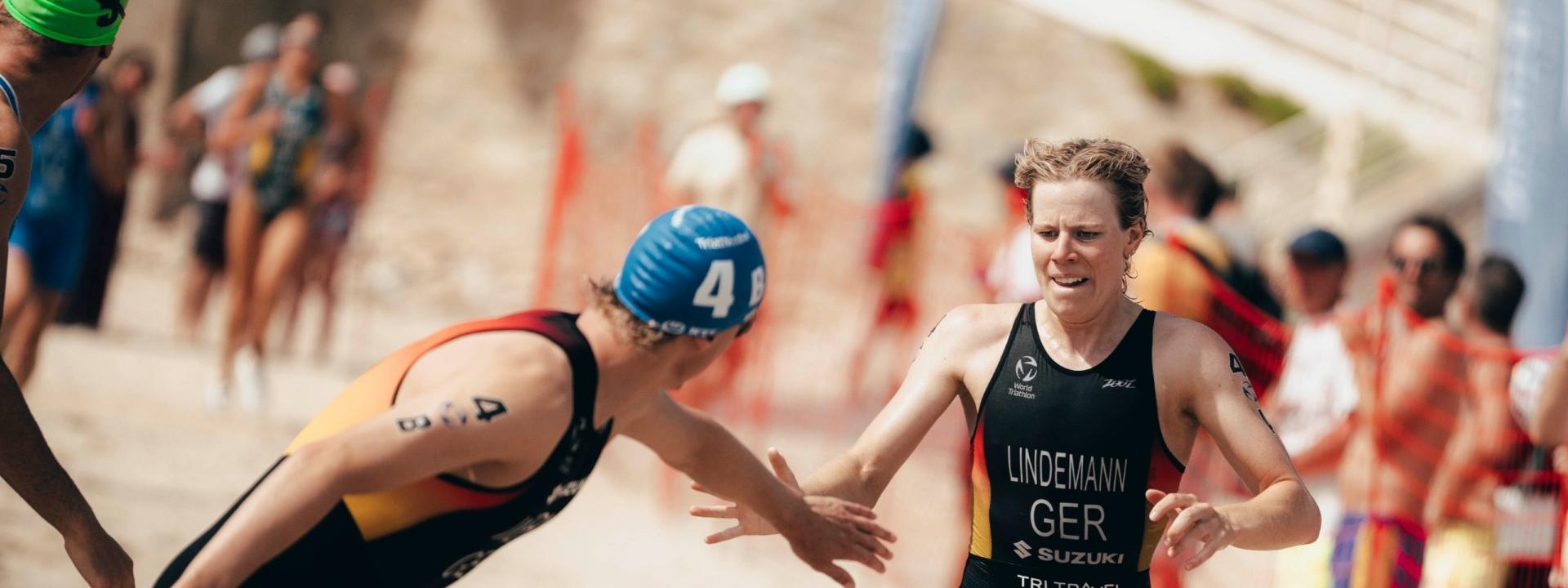Eine Triathletin klatscht mit einem Triathleten ab und schickt ihn im Rahmen einer Staffel auf die Reise