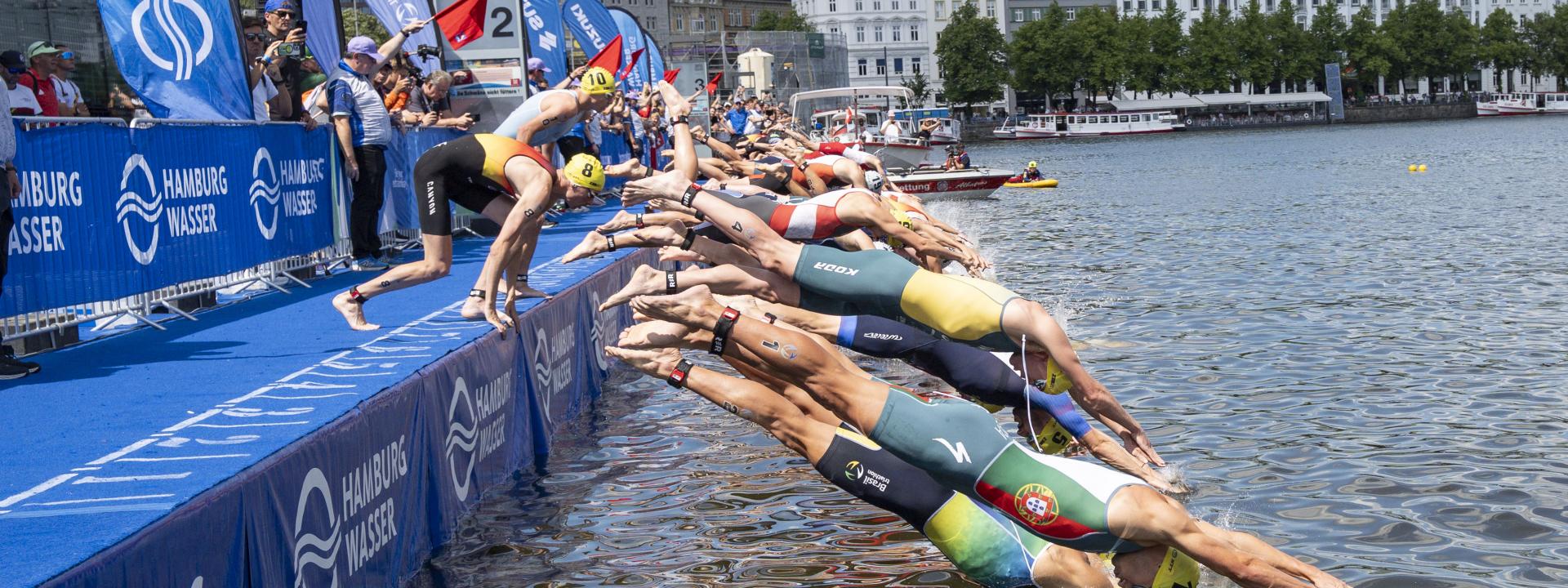Zahlreiche Männer springen bei einem Triathlon nach dem Startschuss ins Wasser