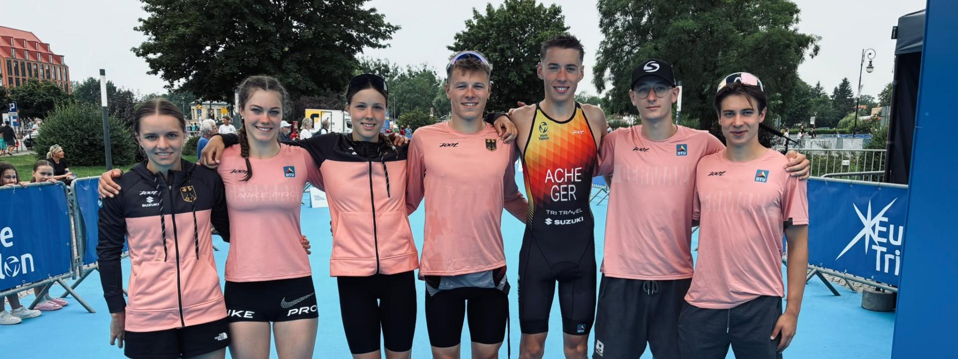 Sieben Nachwuchssportlerinnen und - sportler posieren für ein Gruppenbild vor dem Zielturm einer Triathlonveranstaltung