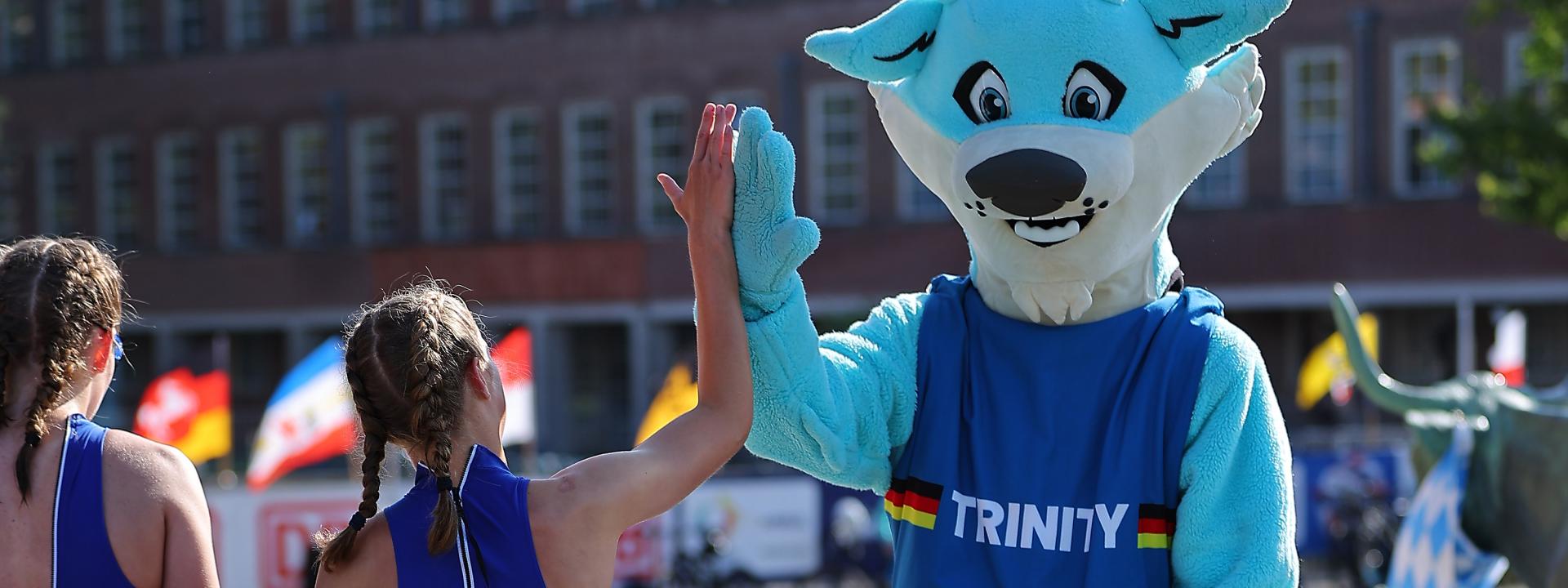 Zwei Schülerinnen klatschen mit dem DTU Maskottchen Trinity ab