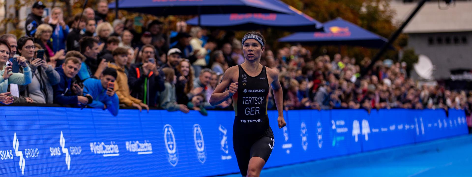 Eine Triathletin läuft auf dem blauen Teppich den Zielkorridor eines Triathlons dem Ziel entgegen