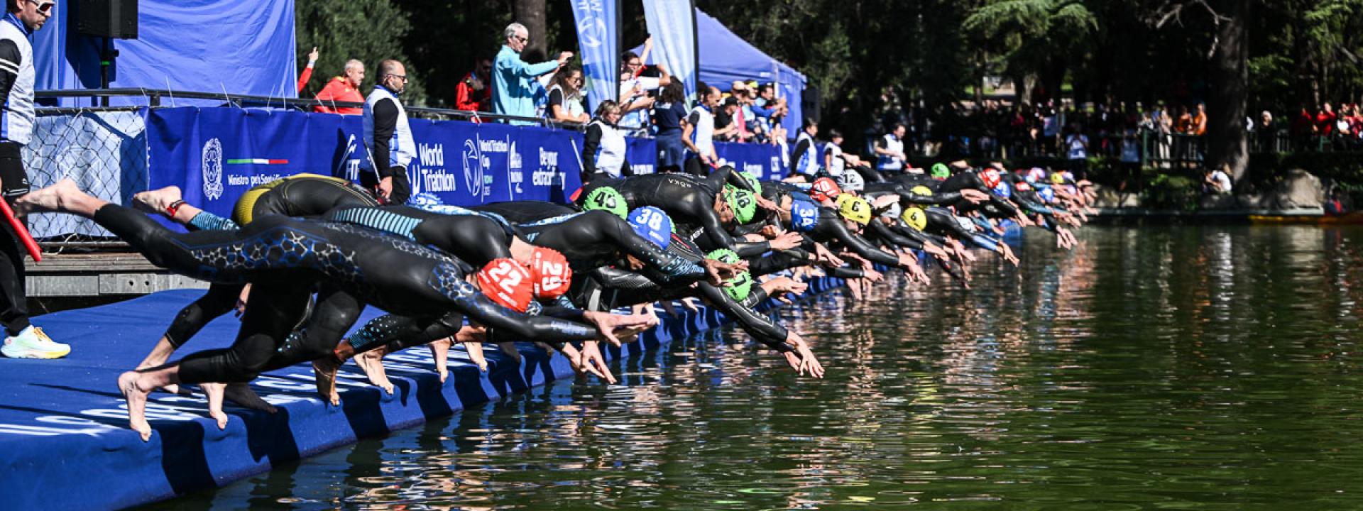 Mehrere Triathleten springen beim Start eines Startes nebeneinander mit einem Kopfsprun ins Wasser