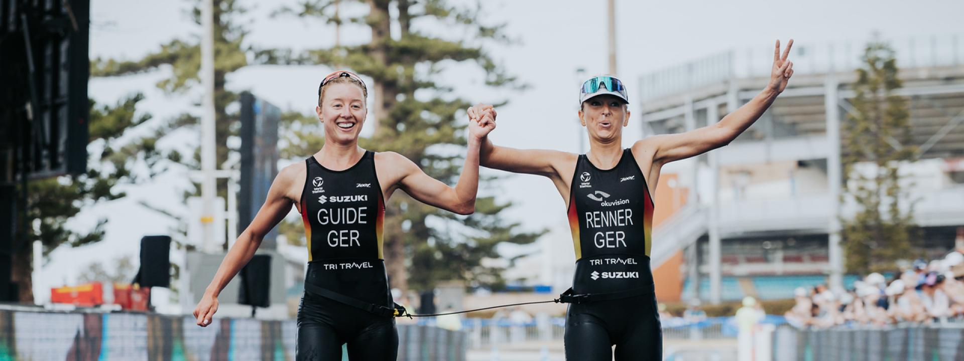 Eine sehbeeinträchtigte Para Triathletin läuft gemeinsam mit ihrer Guide jubelnd über die Ziellinie eine Triathlons