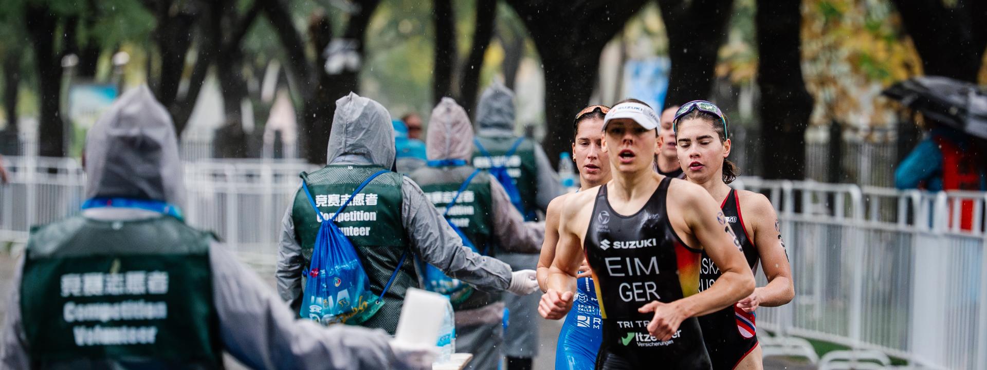 Mehrere Triathletinnen laufen an einer Wasser-Verpflegungsstelle vorbei