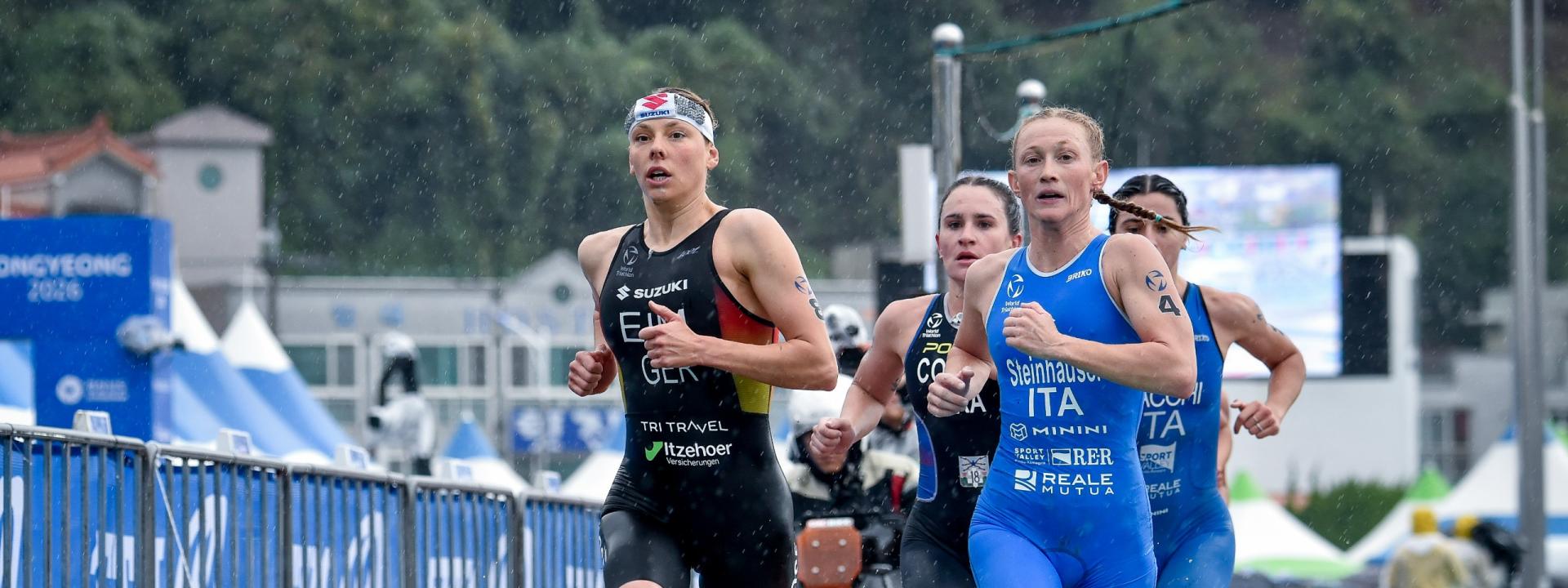 Mehrere weibliche Triathletinnen laufen auf regennasser asphaltierter Straße