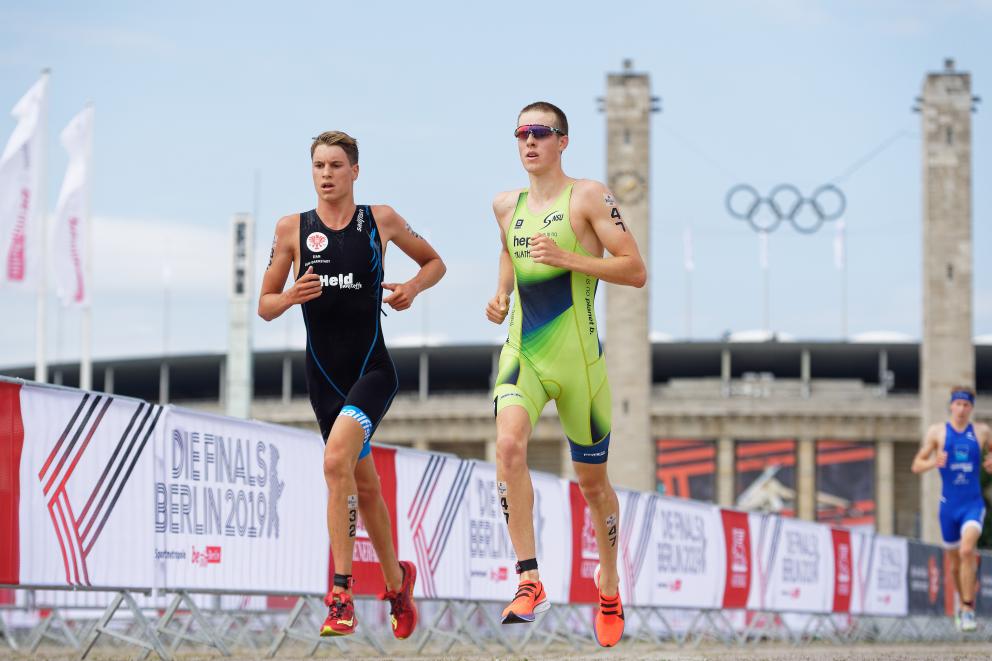 Zwei Triathleten laufen gemeinsam im Hintergrund sind die Olympischen Ringe zu sehen