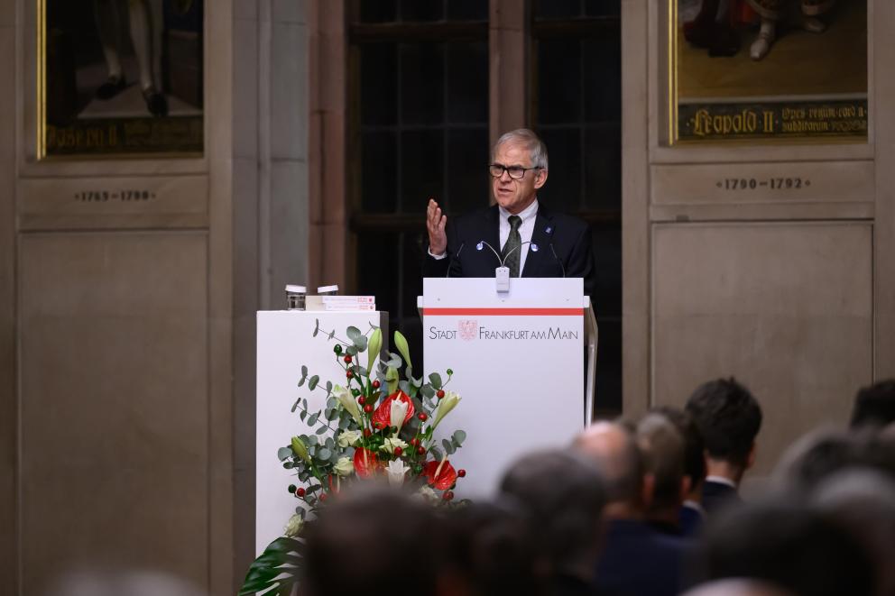 Ein Mann steht am Rednerpult und spricht zu einem Publikum