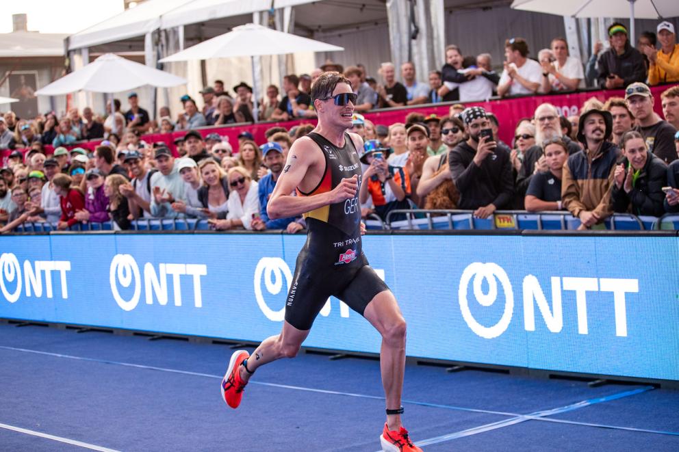 Ein deutscher Triathlet läuft die letzten Meter über den blauen Teppich vor jubelnden Zuschauern ins Ziel