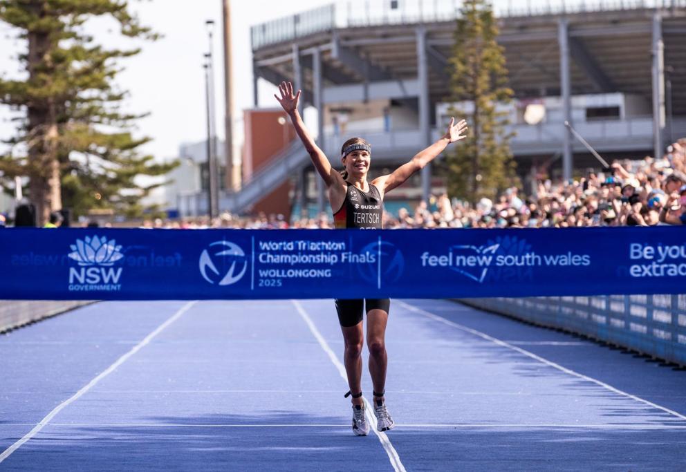 Eine Triathletin läuft mit zum Jubel hochgerissenen Armen als Erste auf das Zielband zu