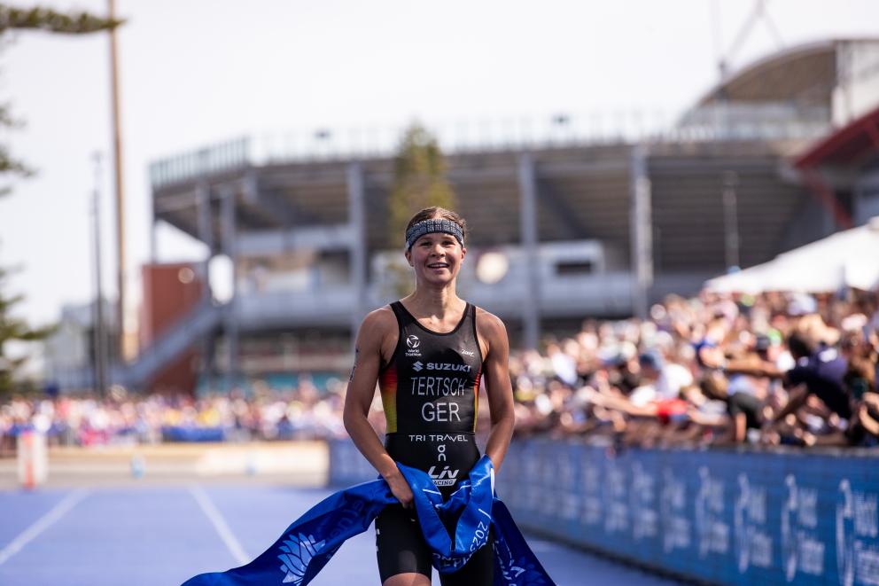 Eine siegreiche Sportlerin steht glücklich im Zielbereich einer Triathlonstrecke