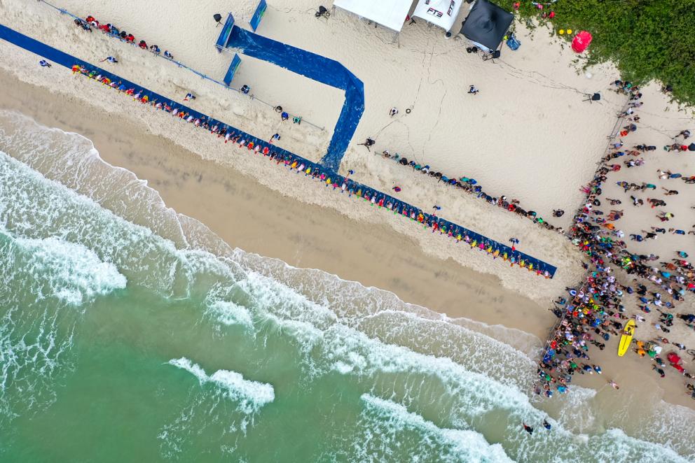 aus der Vogelperspektive sieht man Meer und Strand und einen blauen Teppich auf dem Sand, der die Startlinie für Athleten ist
