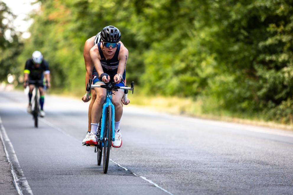 Ein Tandem fährt auf einer Straße, dahinter fährt ein einzelner Radfahrer