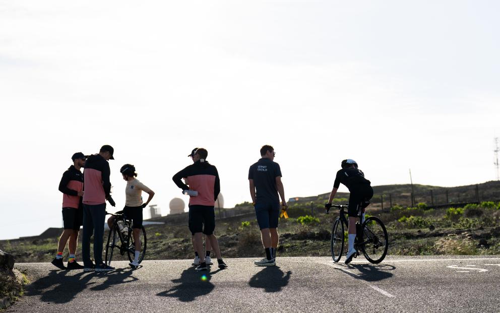 Männliche und weibliche Sportlerinnen und Sportler mit Rennrad analysieren gemeinsam mit mehreren Trainern eine Einheit