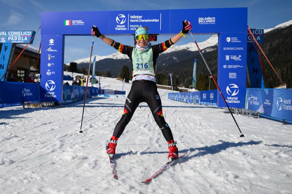 Eine Skilangläuferin freut sich im Ziel und reißt die Arme nach oben