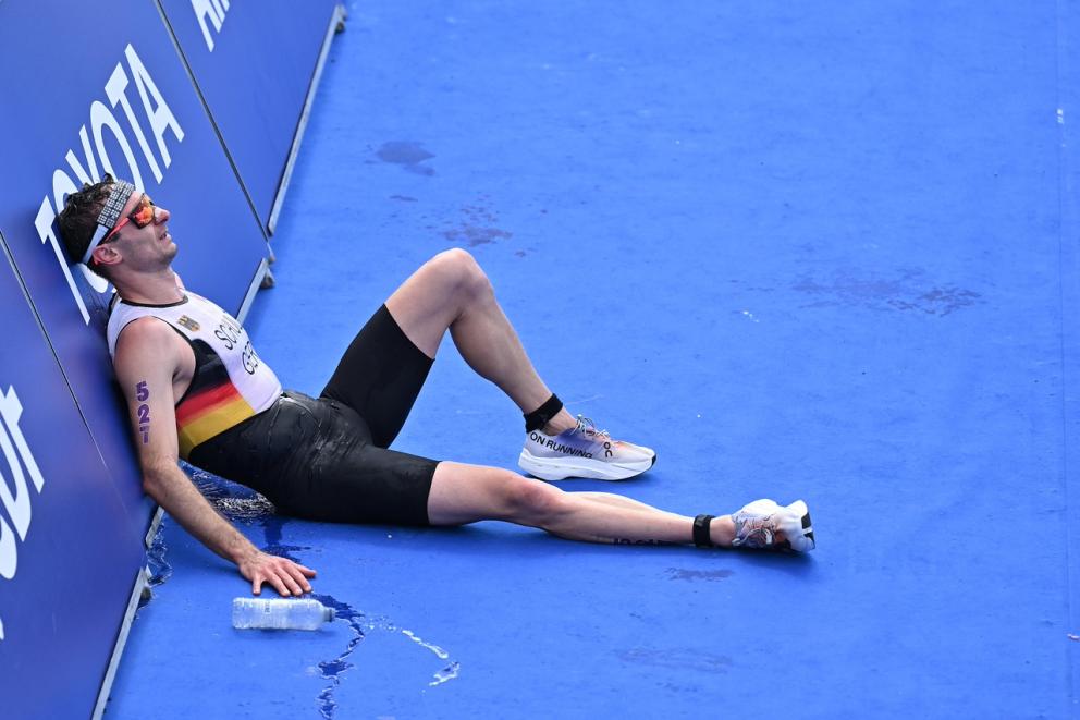 Ein deutscher Para Triathlet sitzt auf dem Boden im Zielbereich und lehnt sich erschöpft an eine Bande an