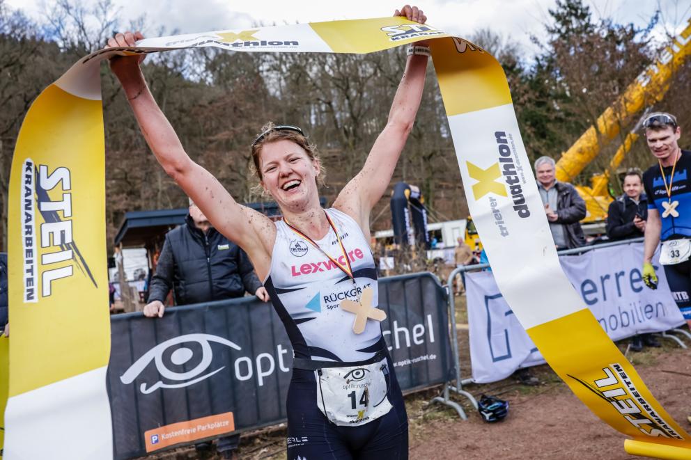 Eine Duathletin jubelt im Ziel mit dem Zielband in der Hand über ihren Sieg