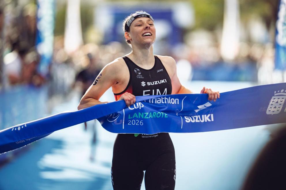 Eine Triathletin läuft glücklich mit dem Zielband in der Hand zum Sieg