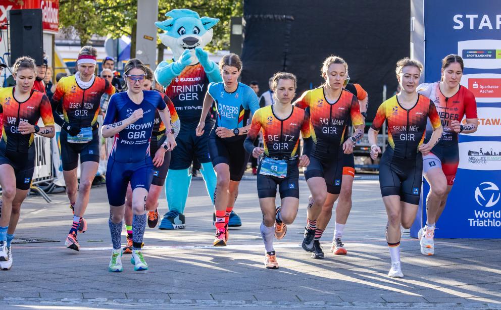 Athletinnen der Duathlon WM in Alsdorf laufen an der Startlinie los, im Hintergrund Maskottchen Trinity