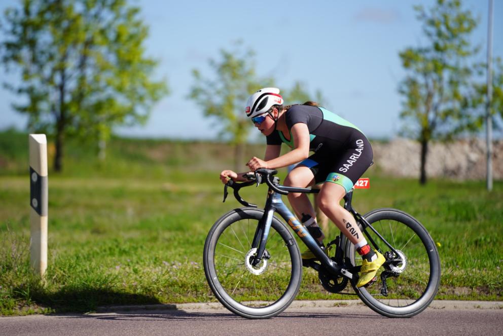 Junge Triathletin auf dem Rennrad mit grüner Wiese und Bäumen