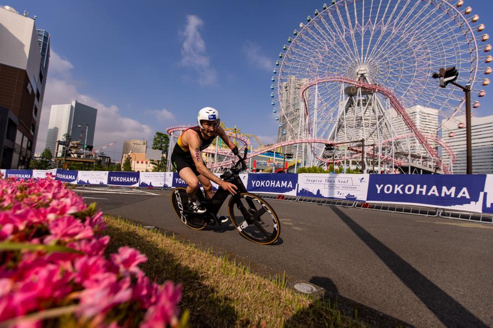 Ein deutscher Para Triathlet fährt mit dem Rad eine Kurve, im Hintergrund ist ein Riesenrad zu sehen
