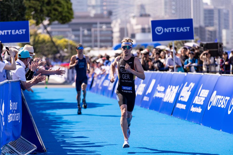 Ein Triathlet läuft auf dem Zielteppich ins Ziel, im Hintergrund folgt ein weiterer Sportler