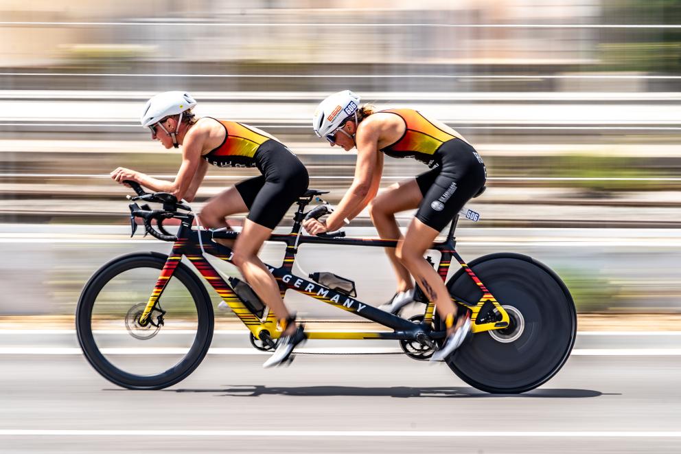 Ein Rennrad-Tandem mit einem Guide und einer sehbeeinträchtigen Sportlerin im deutschen Trikot in rasanter Fahrt