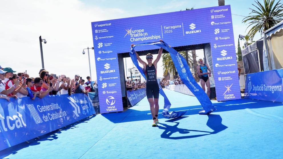 Triathletin läuft mit hochgestreckten Armen und Zielbanner in den Händen unter Zielbogen