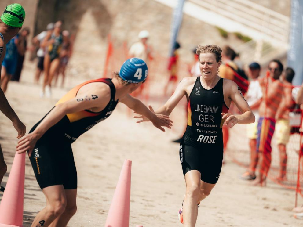 Eine Triathletin klatscht mit einem Triathleten ab und schickt ihn im Rahmen einer Staffel auf die Reise