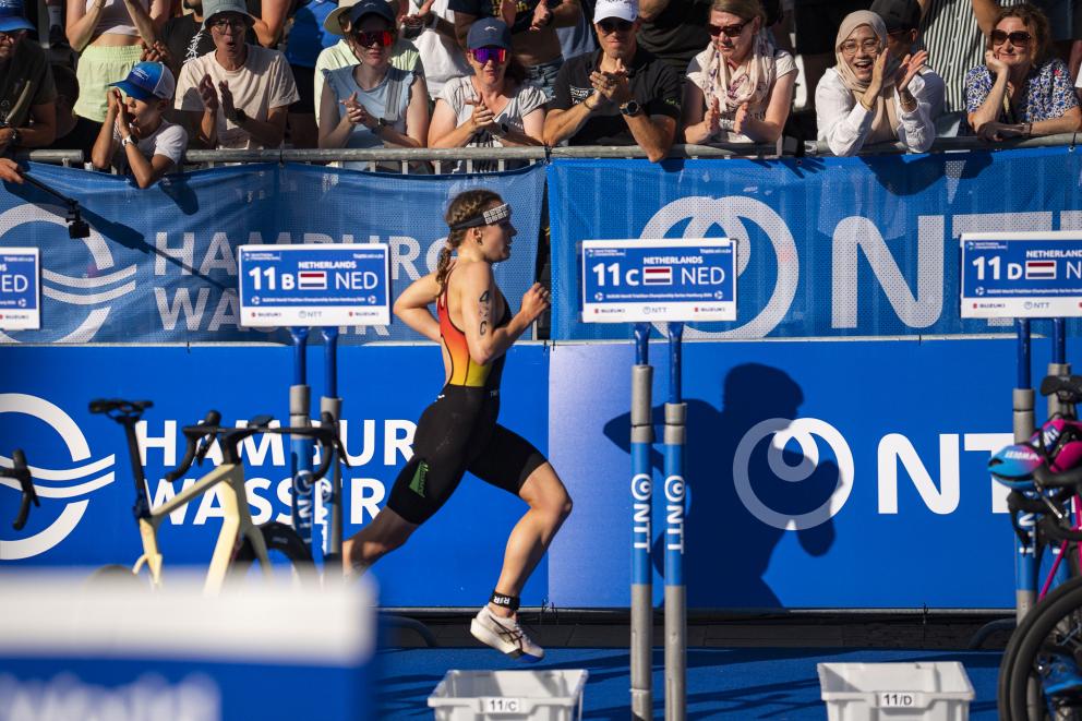 Eine Triathletin läuft vor Publikum durch die Wechselzone
