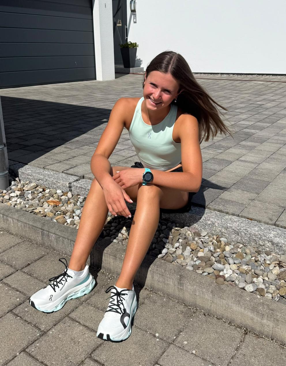 Junge Triathletin sitzt auf Pflasterstein und lacht in die Kamera