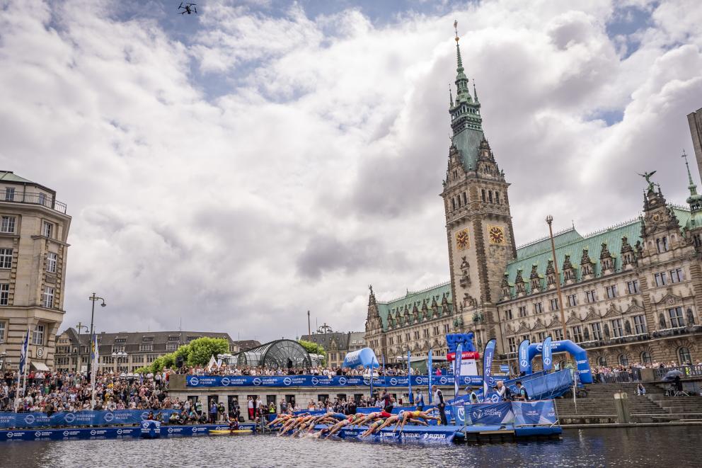 Rund 15 Triathleten springen bei einem Start von einem künstlichen Steg aus ins Wasser