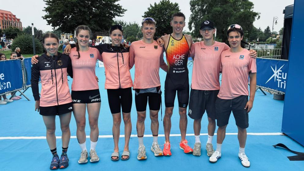 Sieben Nachwuchssportlerinnen und - sportler posieren für ein Gruppenbild vor dem Zielturm einer Triathlonveranstaltung