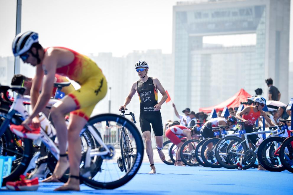 Ein deutscher Triathlet kommt in die Wechselzone eines Triathlon, in der andere Triathleten bereits vom Rad auf das Laufen wechseln