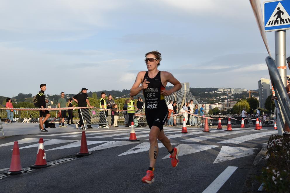 Eine Triathletin läuft auf einer asphaltierten Straße, im Hintergrund schauen Menschen zu