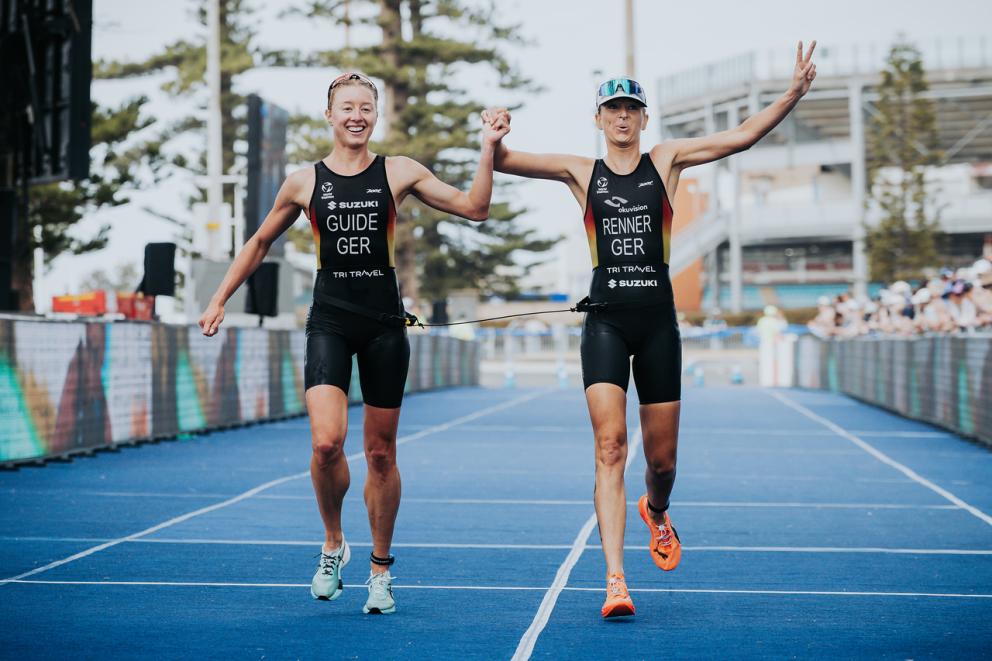 Eine sehbeeinträchtigte Para Triathletin läuft gemeinsam mit ihrer Guide jubelnd über die Ziellinie eine Triathlons